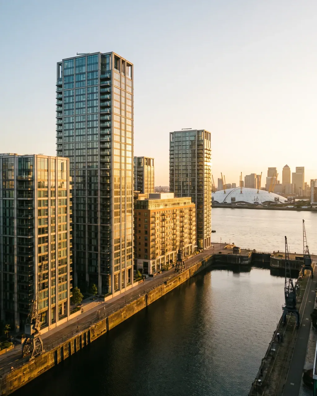 Blackwall glass residential towers on a dockside quay, with the O2 dome and the Canary Wharf skyline across the Thames